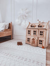 A wooden dollhouse sits in a child's bedroom, surrounded by colorful toys and a cozy atmosphere.
