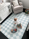  A baby happily plays on a blue and white checkered rug, surrounded by toys and a cheerful atmosphere.