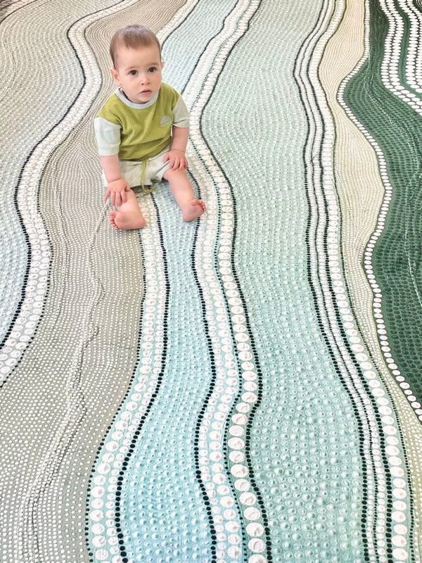 A child sits on a rug patterned with waves, smiling and playing with toys around them.
