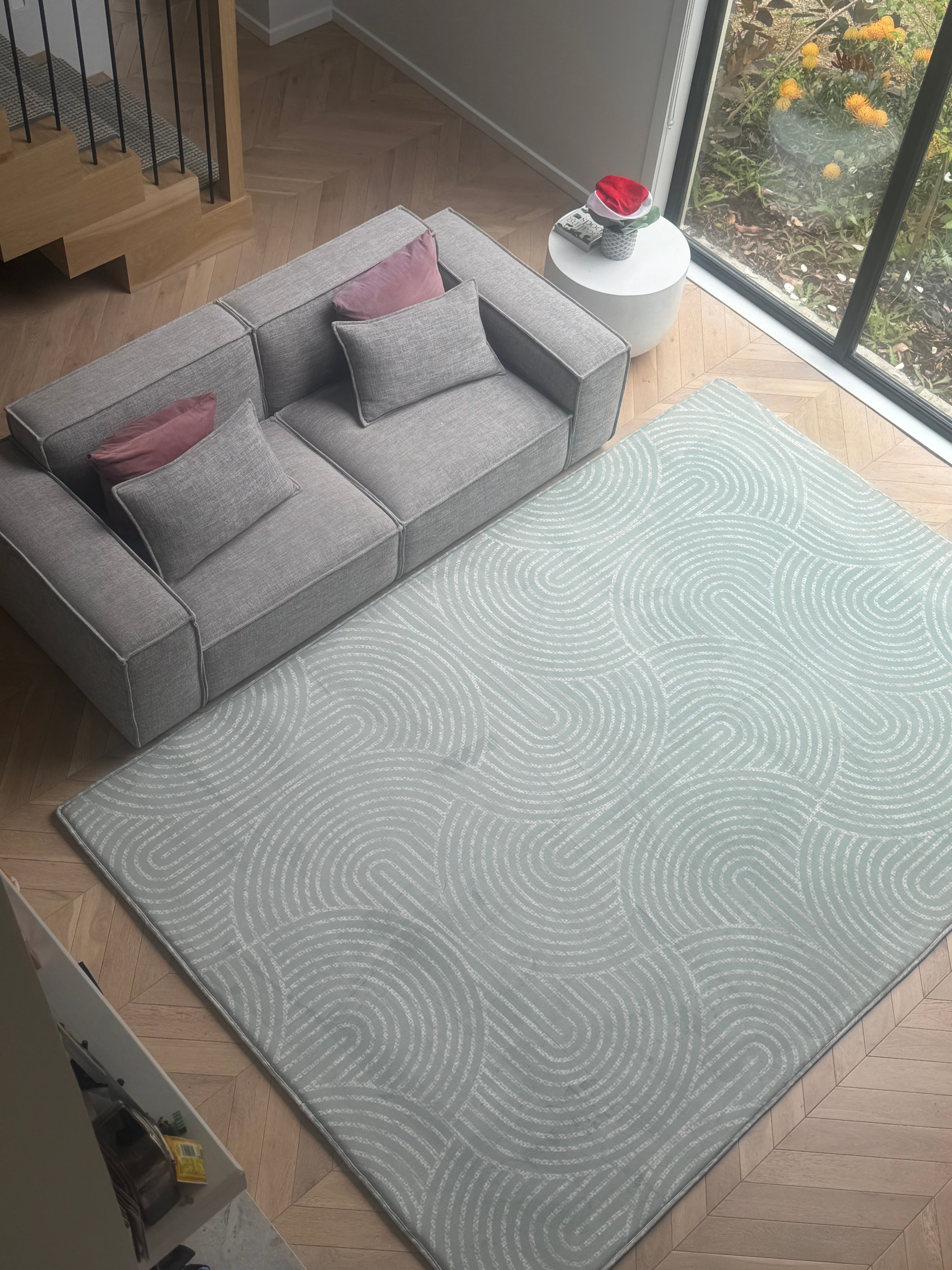 A modern rug in a cozy living room featuring a couch and a large window letting in natural light.