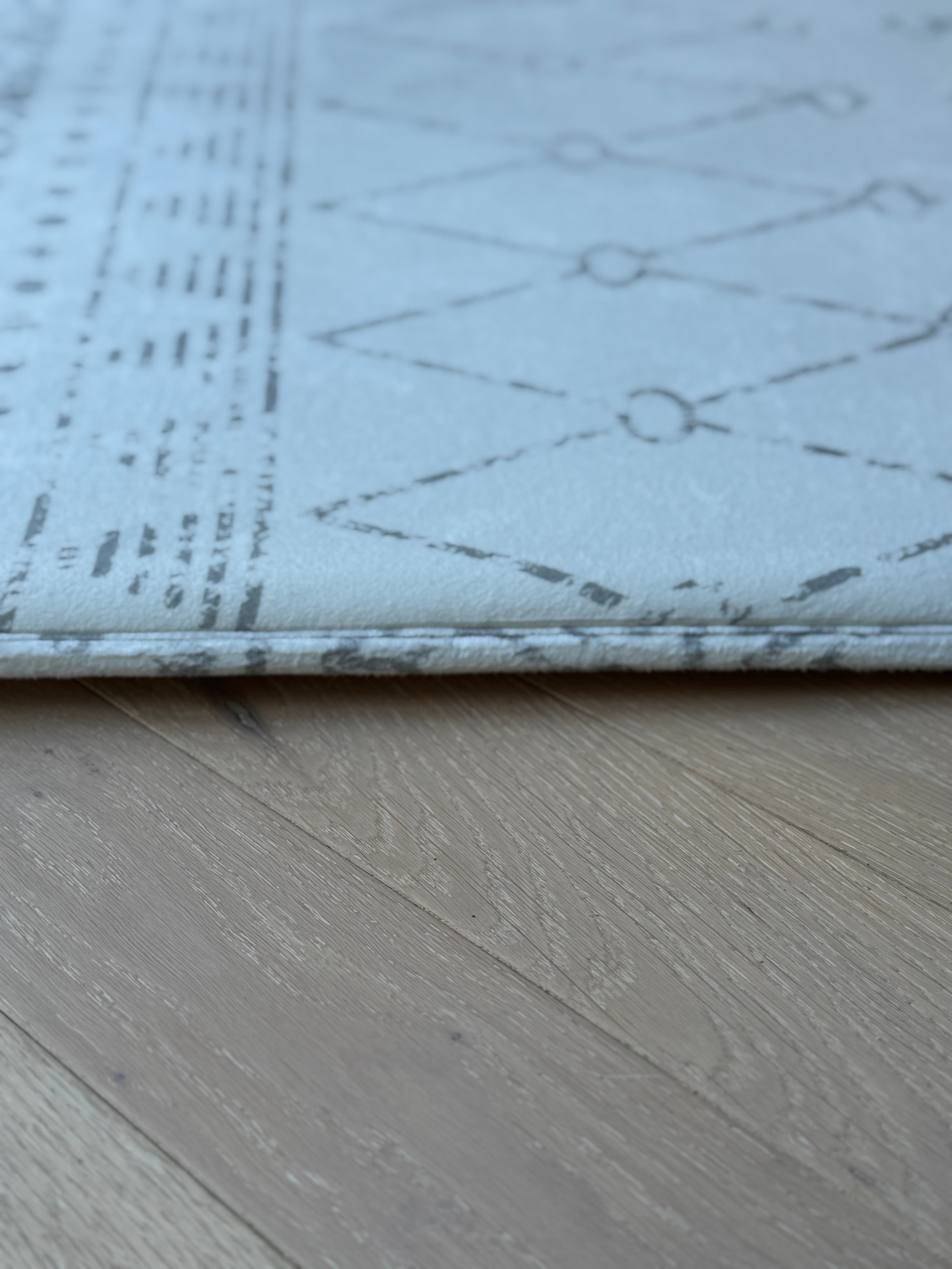 A white rug featuring a geometric pattern, showcasing a modern design suitable for various interior styles.