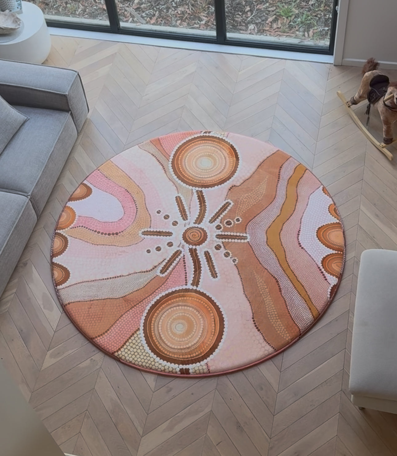 A round memory foam rug with a decorative aboriginal artwork design placed in a cozy living room setting.