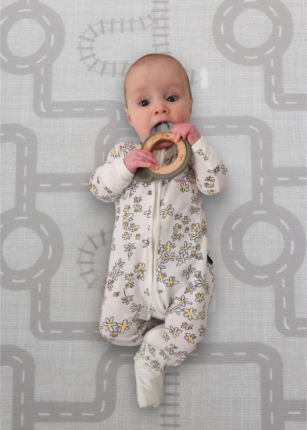 A baby lies on a mat, happily chewing on a colorful toy.