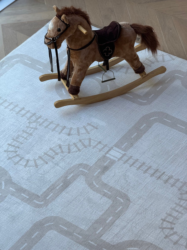 A plush rocking horse sits on a light-colored rug with a printed road and railroad track pattern.